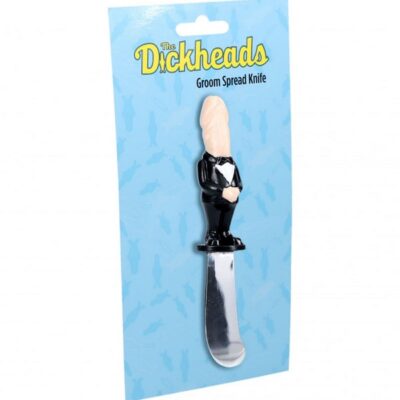 Black metal groom-themed novelty spreader knife by Shots Toys displayed on a charcuterie board